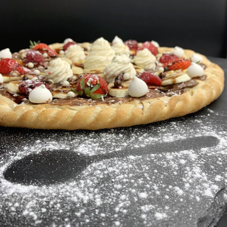Pizza sucrée gourmande garnie de fraises, bananes, meringues et chocolat, réalisée lors d’un atelier à l’école de pizza du Chef Rabah Zaoui.