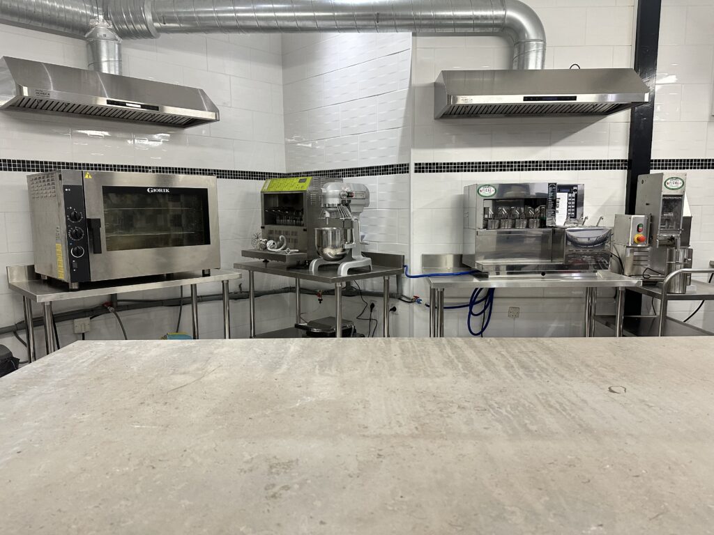 Salle de préparation avec plateau technique, incluant four, machine à pâtes et robot culinaire.